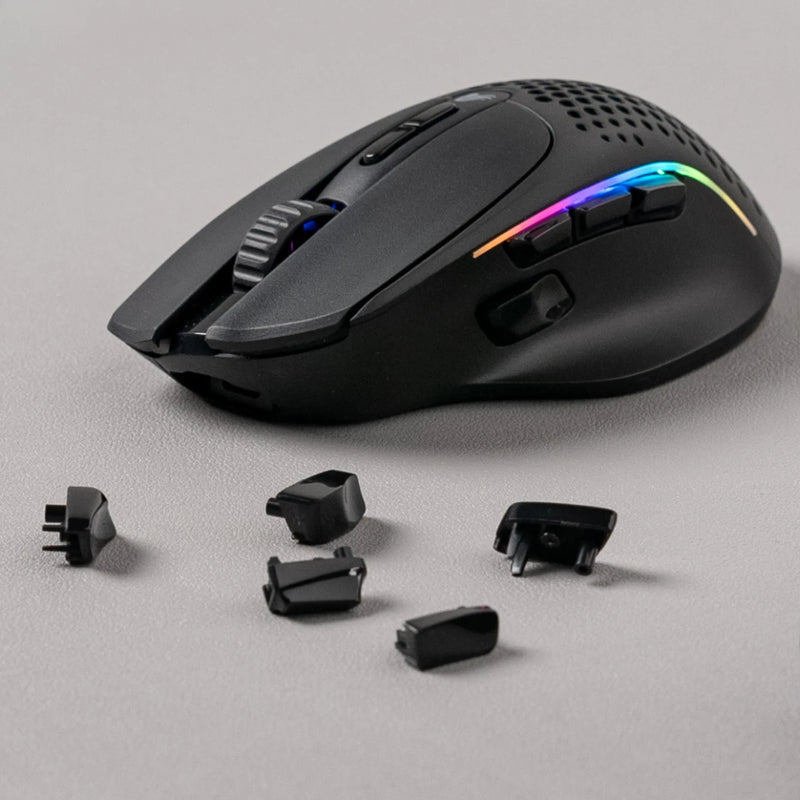 A black Model I 2 Wireless gaming mouse with customizable side buttons and RGB lighting is placed on a gray surface. Several detachable button pieces are positioned around the mouse.