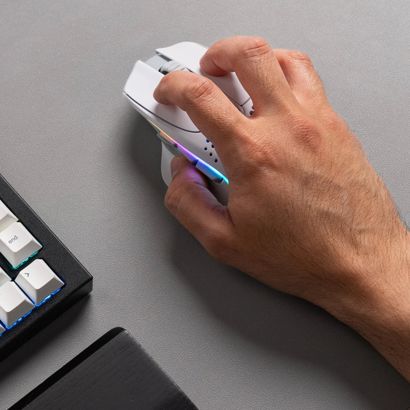 A top-down view of a hand using a claw grip to hold a Model I 2 Wireless in White on top a grey mousepad. A GMMK PRO 75% and black wooden wrist rest are partially visible on the side.