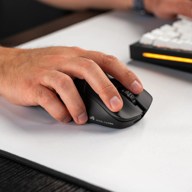 A close-up of a hand using a Model D 2 PRO Series Wireless Mouse on a white mousepad, with a GMMK PRO 75% partially visible in the background.