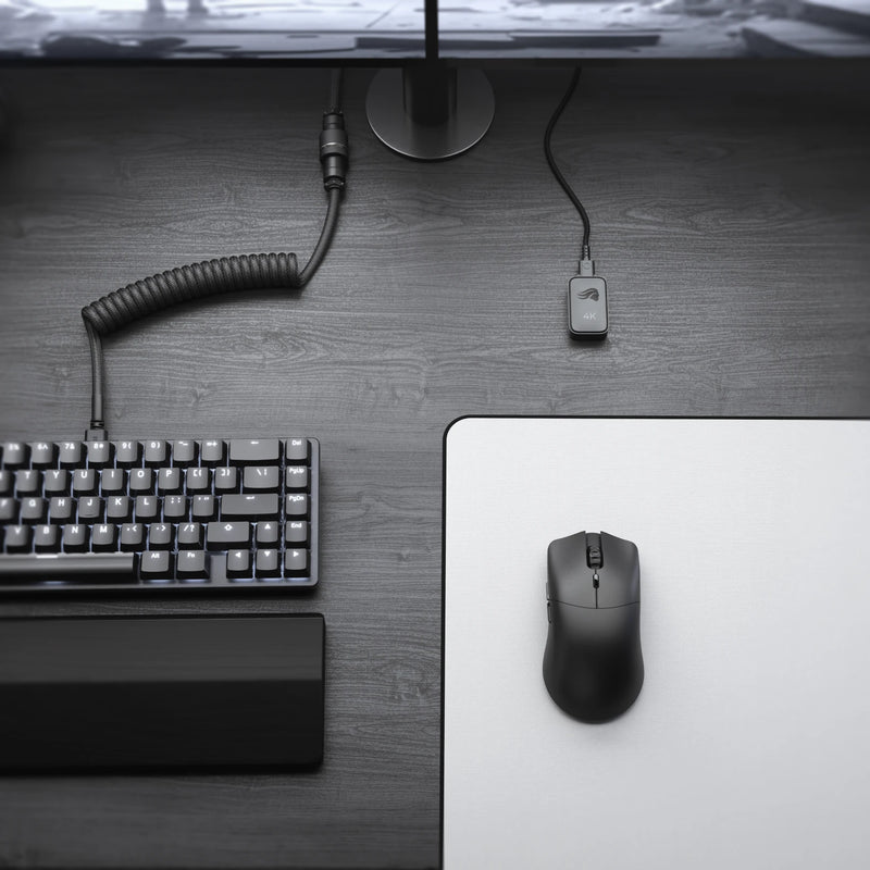 A top-down view of a Model O 2 PRO Series Wireless Mouse 4K/8KHz Edition on a white mouse pad, and a GMMK 2 65% in Black on a dark wooden desk. A monitor stand, cables, and 2.4GHz 4KHz Wireless Receiver are also visible.