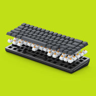 A Black GMMK 2 65% Barebones with GPBT Black Ash Keycaps is shown in an exploded view, revealing Glorious Panda switches beneath the keys. The background is a bright lime green.
