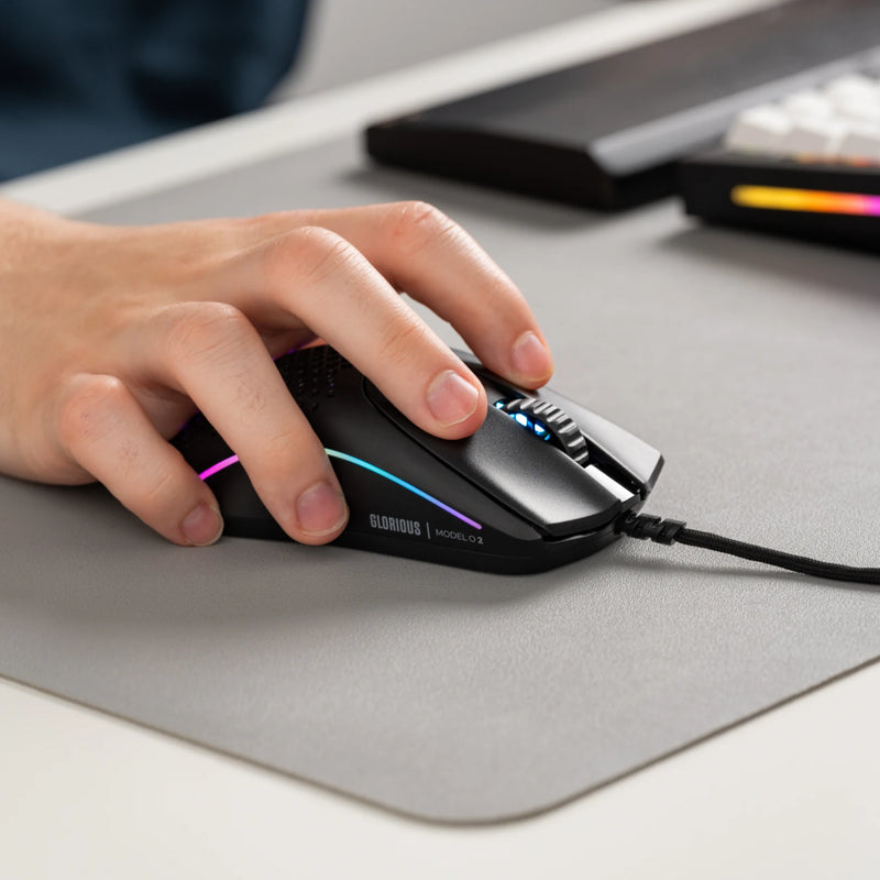 Right side view of a hand using a Model O 2 Wired in Black on top of a grey mousepad next to a GMMK PRO and wooden wrist rest