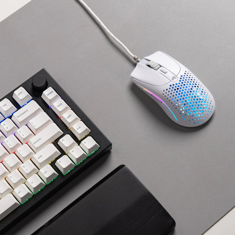 A top-down view of a Model O 2 Wired in White on top a grey mousepad. A GMMK PRO 75% and black wooden wrist rest are partially visible on the side.